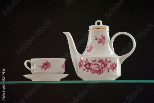 white teapot and a cup of tea with beautiful red flowers on a black background