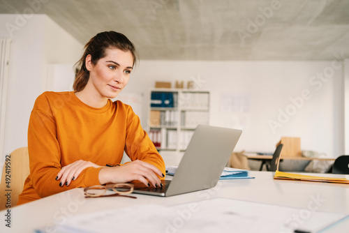 Young businesswoman smiling as she works on a laptop sitting in an modern office