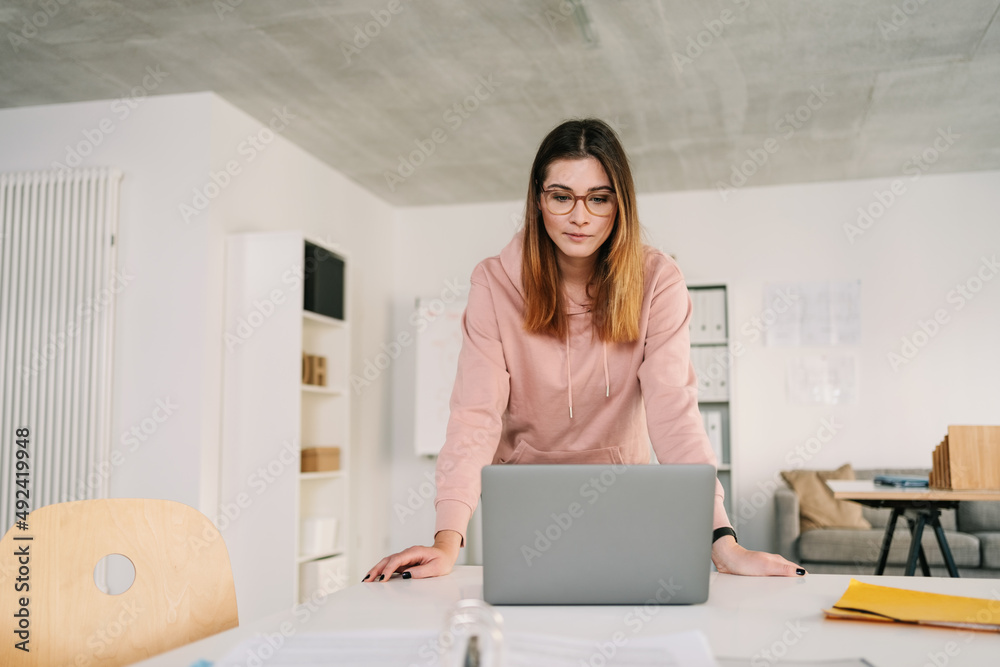 Young business woman standing in her office looking at laptop. Young business woman standing in her office looking at laptop.