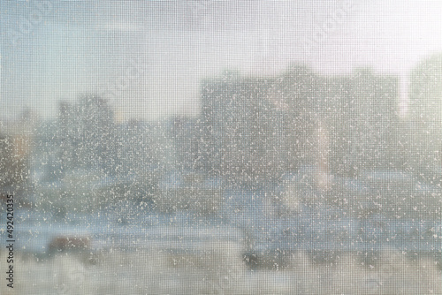 Snow flakes in winter on the mosquito net on the balcony. Behind the grid is a sunny, clear day in the city.