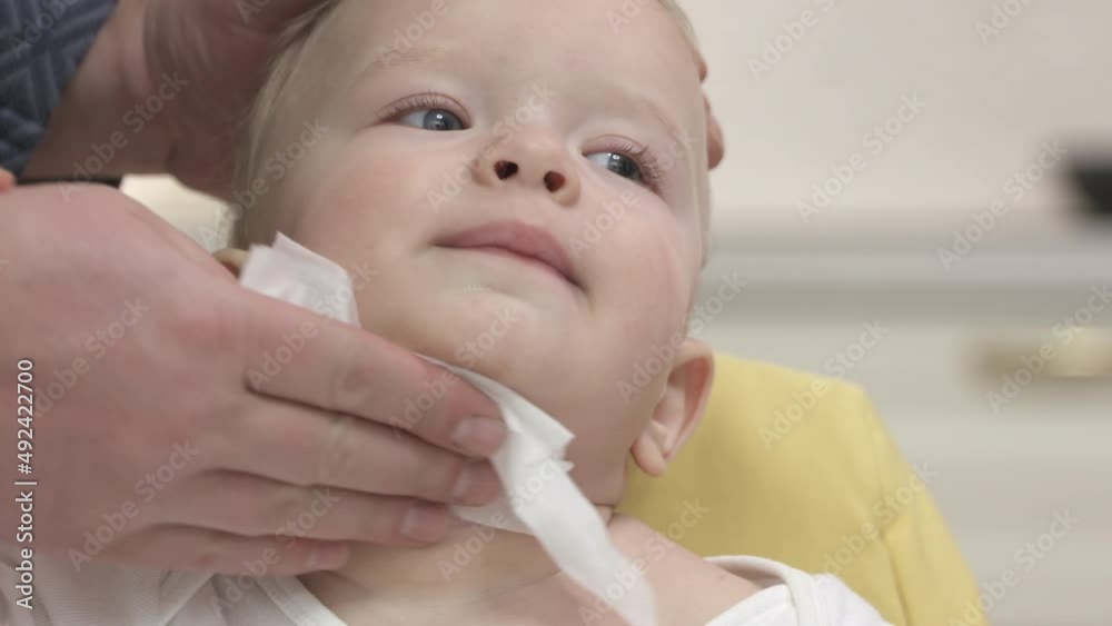 Father wiping face of his one-year-old son with baby wipes after feeding him in the kitchen. High quality 4k footage Father wiping face of his one-year-old son with baby wipes after feeding him in the kitchen. High quality 4k footage