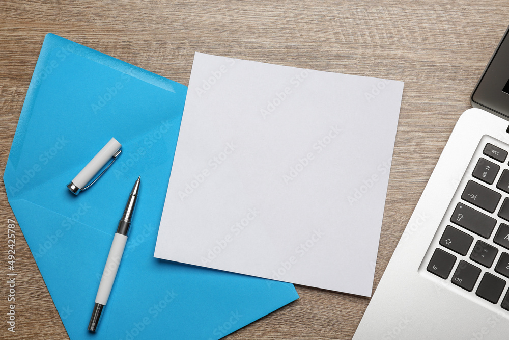 Light blue envelope with blank letter, pen and laptop on wooden table, flat lay Light blue envelope with blank letter, pen and laptop on wooden table, flat lay