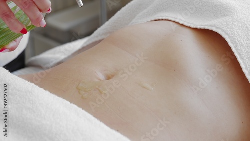 Pouring massage oil on attractive belly of young slim woman. Concept of body care and alternative medicine