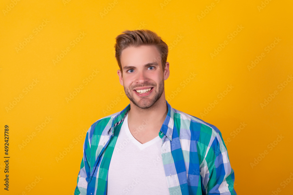 Handsome caucasian unshaven guy portrait happy smiling in checked shirt yellow background, man