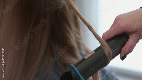 Close-up of a woman's hand curling her hair with a flat iron. Beautiful girl at the hairdresser. Beauty salon