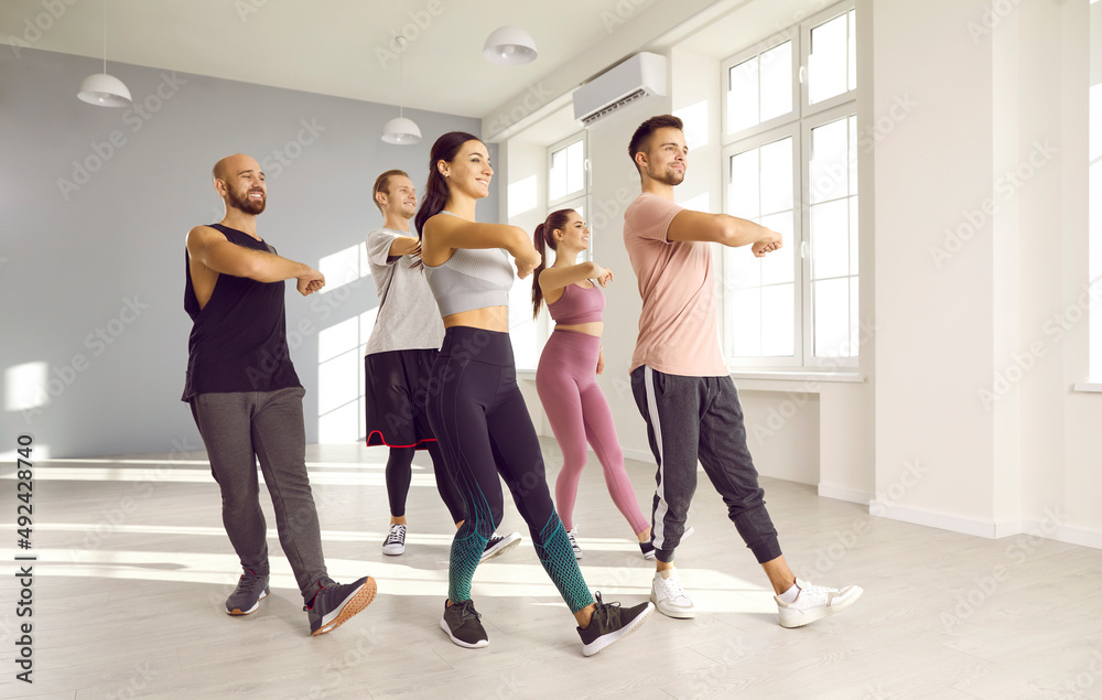 Fototapeta premium Group of happy, energetic, fit people doing physical exercises at a modern gym. Team of cheerful, smiling young men and women enjoying a dance class or an active fitness workout together