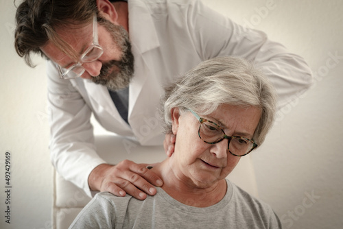 Caucasian senior woman suffering from cervical arthrosis relies on the assistance hands of her physiotherapist