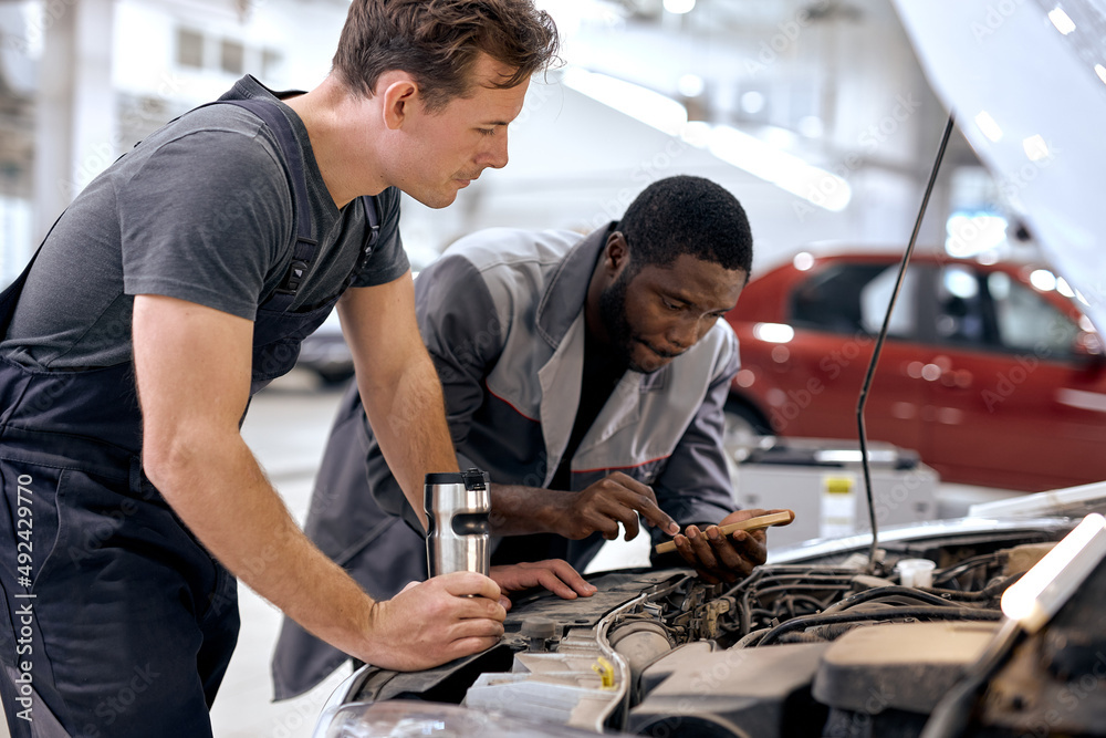 diverse Caucasian and black Men mechanic inspection checking bug in engine from application smartphone. white car for service maintenance insurance with car engine.for transport automobile automotive diverse Caucasian and black Men mechanic inspection checking bug in engine from application smartphone. white car for service maintenance insurance with car engine.for transport automobile automotive