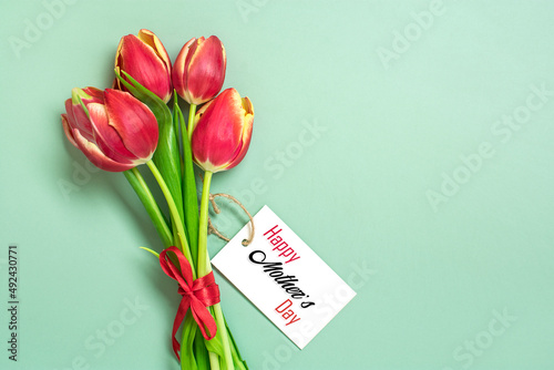 Bouquet of red tulips, text Happy Mother's Day on card on green background Top view Flat lay Holiday greeting card