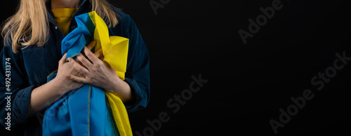 Woman holds ukrainian blue and yellow flag on black background, copyspace blank photo