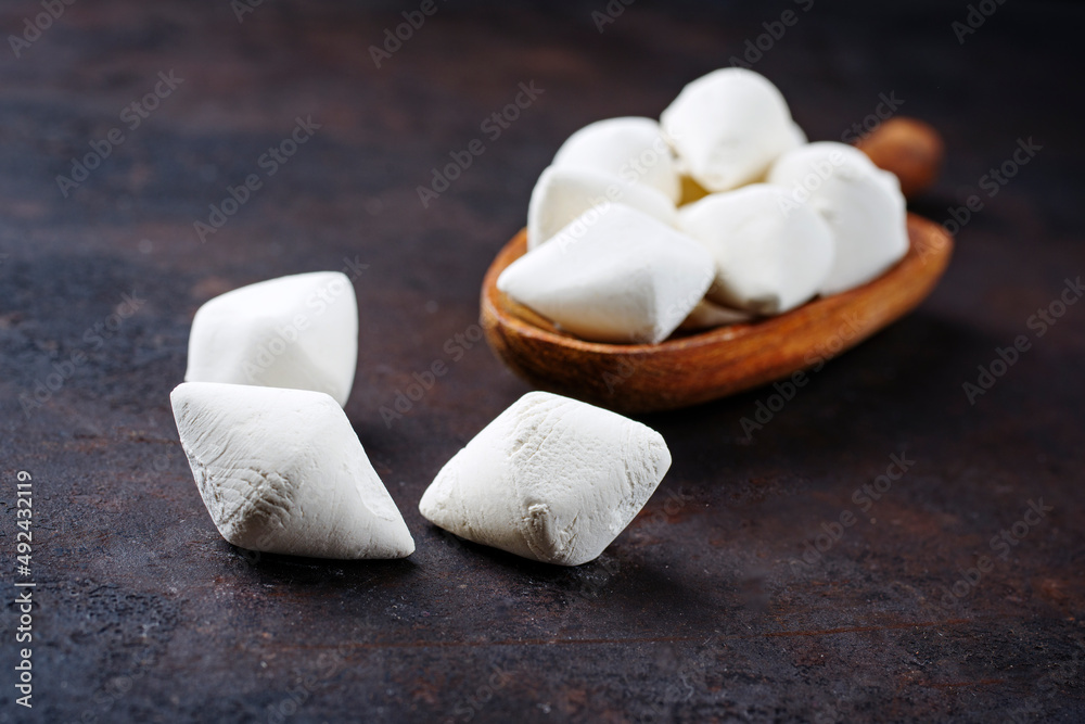 Traditional Afghan dried curd kashk pieces on a small wooden shovel as close-up on black rustic background with copy space Traditional Afghan dried curd kashk pieces on a small wooden shovel as close-up on black rustic background with copy space