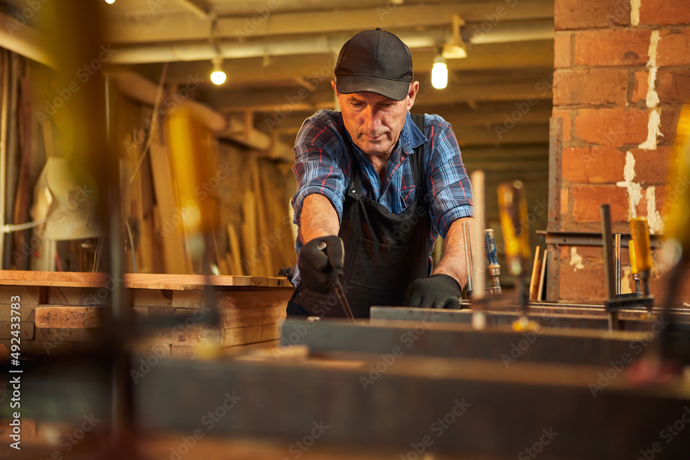 Portrait of a senior carpenter in uniform gluing wooden bars with hand pressures at the carpentry manufacturing Portrait of a senior carpenter in uniform gluing wooden bars with hand pressures at the carpentry manufacturing