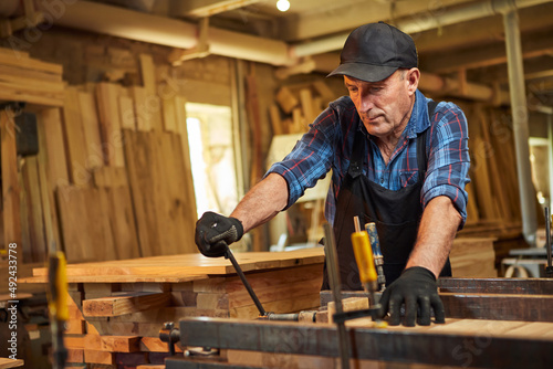 Portrait of a senior carpenter in uniform gluing wooden bars with hand pressures at the carpentry manufacturing