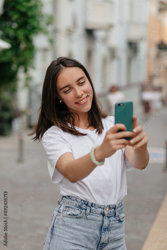 Charming lovely lady with dark hair wearing white t-shirt is sitting in open air cafe in the city in warm spring day. Outside portrait of lovely smiling girl
