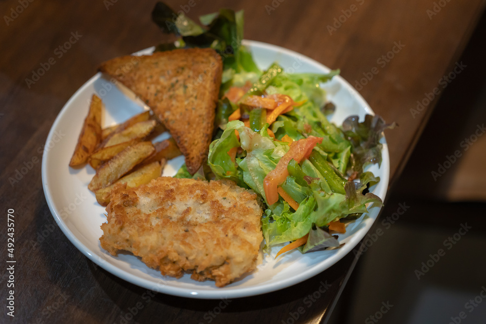 delicious homemade menu, Fried Sea Bass fish fillet in breadcrumbs, buttered bread and fresh vegetable salad served with French Fries on an old wooden table 