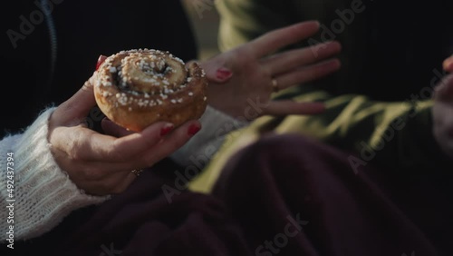 Girl eating delicious cinnamon bun while talking group of friends discussing food baking bakery bake cookie dough buns freshly made pie desert hanging out tea European teen woman hand hands photo