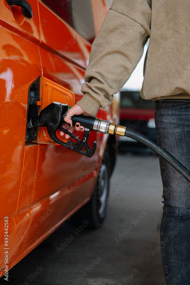 Woman's hand filling the tank of her vehicle with the hose at the gas station