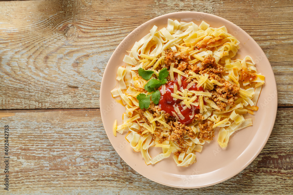 Pasta bolognese garnished with herbs and cheese in a plate on a wooden table. save a place. Pasta bolognese garnished with herbs and cheese in a plate on a wooden table. save a place.