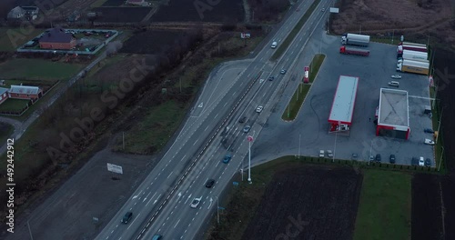 a four-lane automobile highway outside the city in a populated industrial area along which a stream of cars drives passing a gas station. drone view