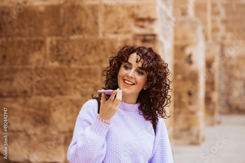 Young woman with curly hair using her smartphone outdoors, sending an audio. Technology portrait. Isolated woman
