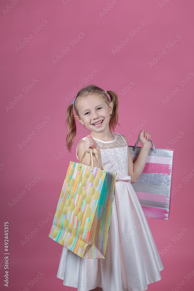 Cute little girl in a party dress on pink background holding colorful bags