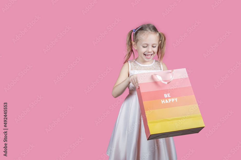 Fototapeta premium Adorable girl holding shopping bags against pink background with copy space.