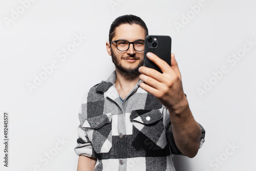 Photo of attractive young guy, in plaid shirt taking selfie on smartphone.