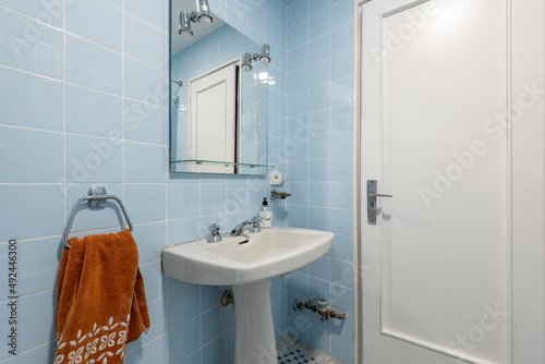 Toilet with blue square tiled walls  white wooden door and white toilets