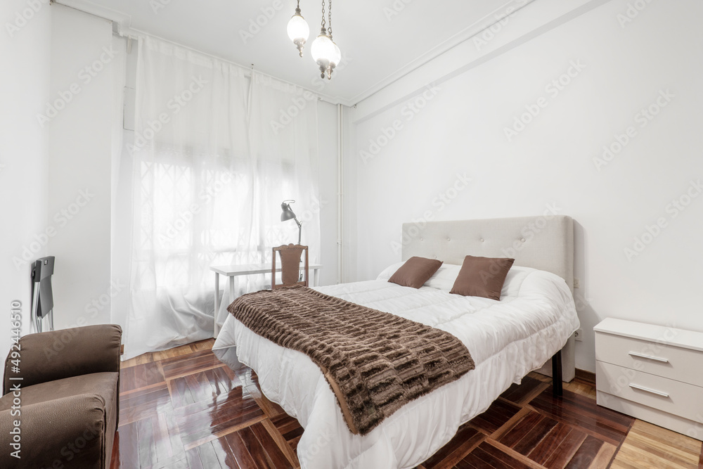 Bedroom with bed with white duvet, brown blanket with matching cushions, white study table and oak parquet Bedroom with bed with white duvet, brown blanket with matching cushions, white study table and oak parquet