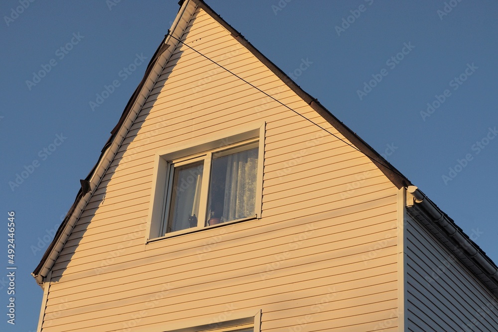 brown plastic attic of a private house with one window on the street against a blue sky brown plastic attic of a private house with one window on the street against a blue sky