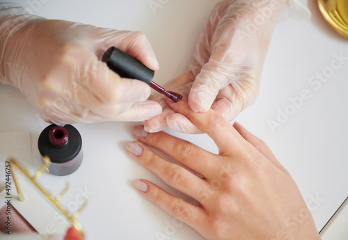 Fotografiet Close up of manicure specialist hands in sterile gloves applying red nail polish on woman fingernail