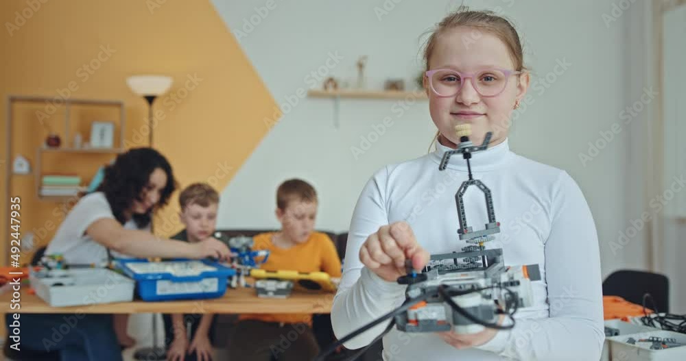 Smiling preteen child demonstrating handmade construction toy in robotics workshop while showing thumb up and looking at camera Smiling preteen child demonstrating handmade construction toy in robotics workshop while showing thumb up and looking at camera