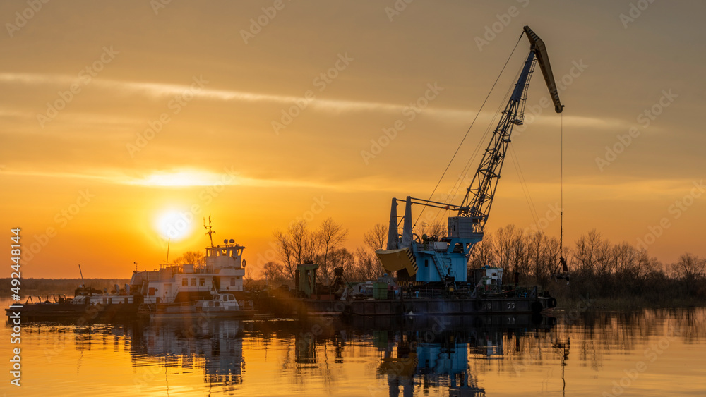 Vessel engaged in dredging at sunset time. Ship excavating material from a water environment.