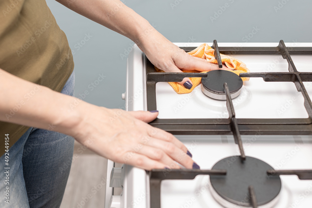 woman wiping a gas stove burner with a rag