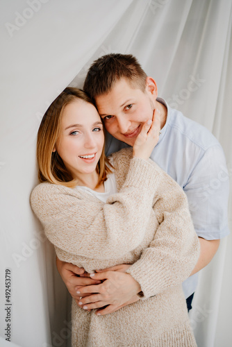 a happy and loving couple hugs against the background of a white curtain. 