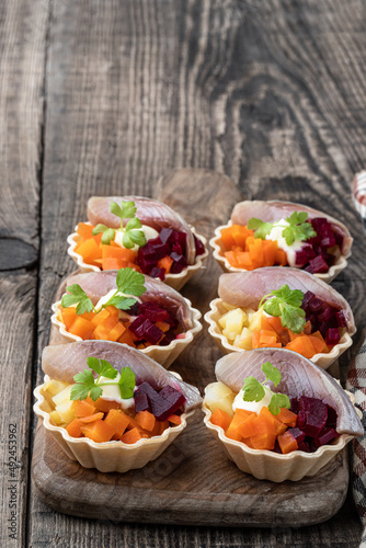 Herring salad with colorful vegetables in small tartlet on wooden table