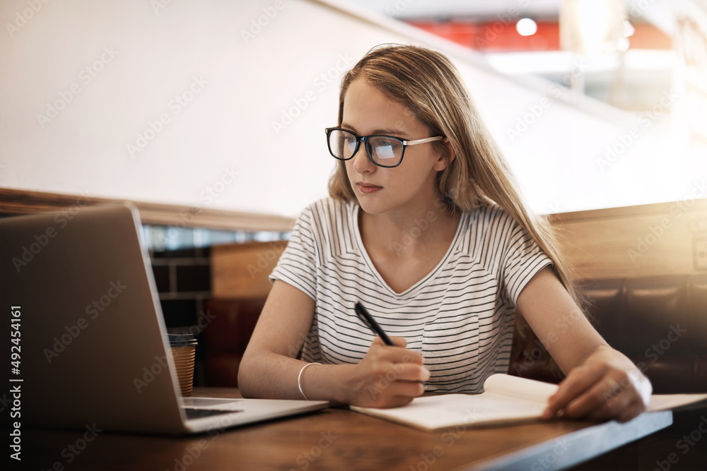 Getting ready for finals. Cropped shot of a focussed young student using her laptop to study at a table in a cafe. Getting ready for finals. Cropped shot of a focussed young student using her laptop to study at a table in a cafe.