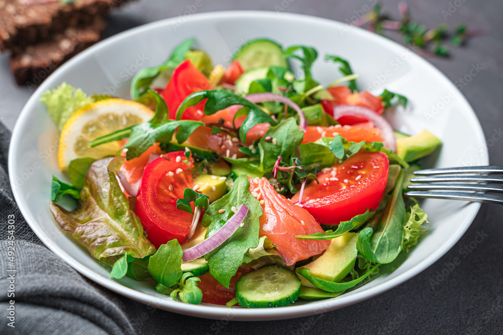 Salad with salmon and avocado on a dark background.
