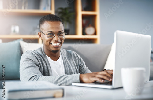 I stay connected so I dont miss out on anything. Portrait of a happy young man using a laptop while relaxing at home.