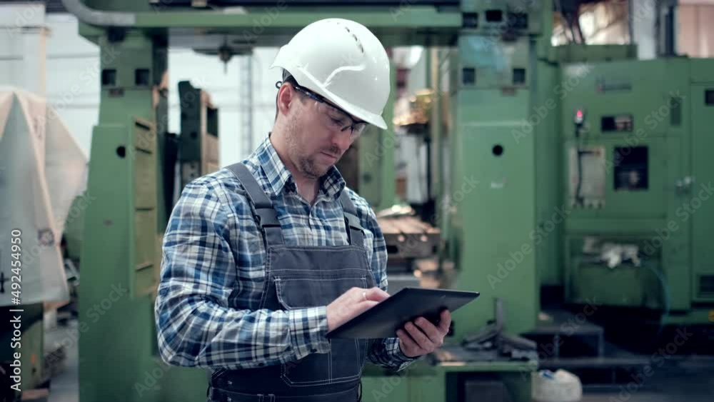 Shot of Professional Factory Worker Wearing Hard Hat Holds Tablet Computer, Walking Thorugh Modern Industrial Manufacturing Facility Shot of Professional Factory Worker Wearing Hard Hat Holds Tablet Computer, Walking Thorugh Modern Industrial Manufacturing Facility