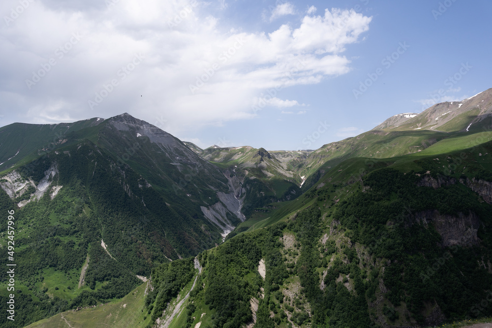 the Kazbegi mountain ranges in Georgia are green and have a clear sky above them.