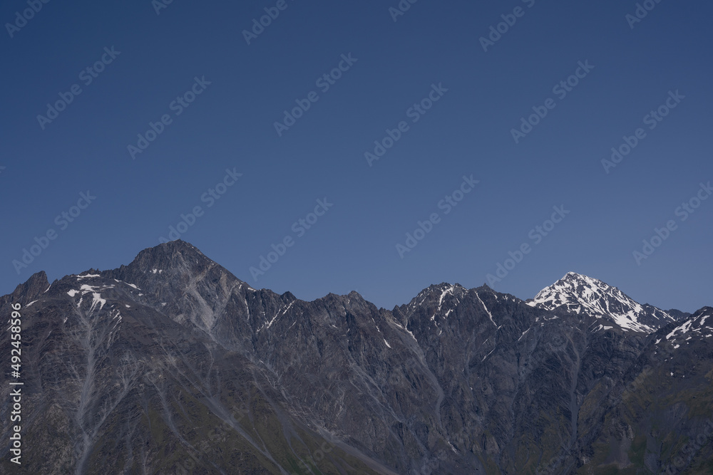 dramatically dark gray mountains with a bit of white snow on the tops, behind which a dark blue sky opens