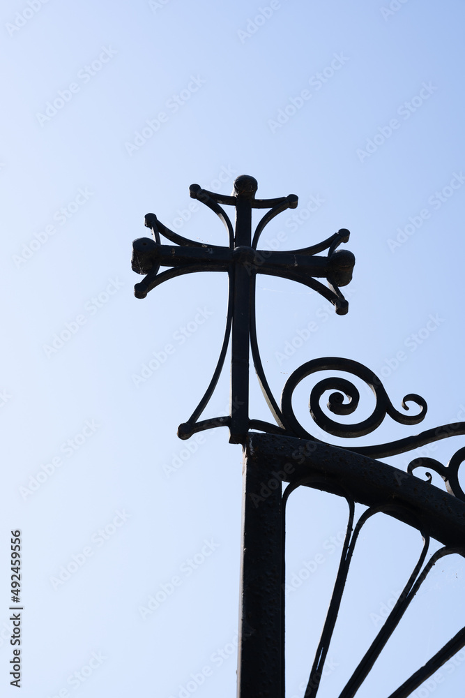wrought metal gates with a cross of believers at the very end, with a light blue sky in the background wrought metal gates with a cross of believers at the very end, with a light blue sky in the background
