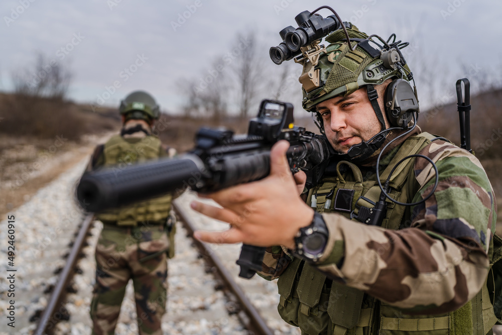 Two soldiers dogs of war mercenaries men in uniform armed service rifles aiming gun while securing the railroad in combat zone in war military battle observing territory patrolling area during mission Two soldiers dogs of war mercenaries men in uniform armed service rifles aiming gun while securing the railroad in combat zone in war military battle observing territory patrolling area during mission