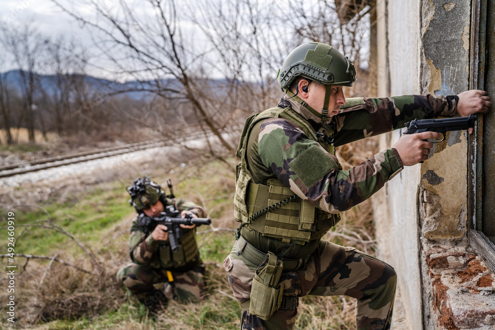 Two men soldiers in uniform braking in to the house ruin during mission battle operation dogs of war volunteers mercenaries contractor secure the building armed service holding rifles pointed