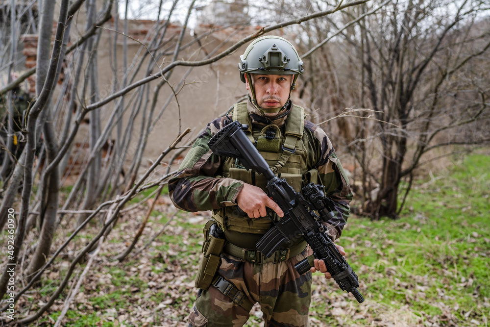 one man front view portrait of soldier in camouflage uniform armed with rifle ready to go on a mission in war zone standing outdoor in nature looking to the camera dogs of war mercenaries or volunteer