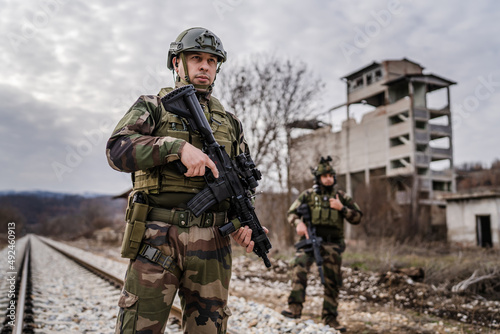 Two soldiers dogs of war mercenaries men in uniform armed service rifles standing while securing the railroad in combat zone in war military battle observing territory patrolling area during mission