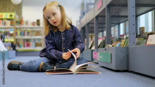 Adorable 4 year old girl in municipal library and reading a book. Literature for children