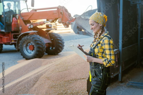Grain being stored in granary or storage house with farmer keeping track taking notes