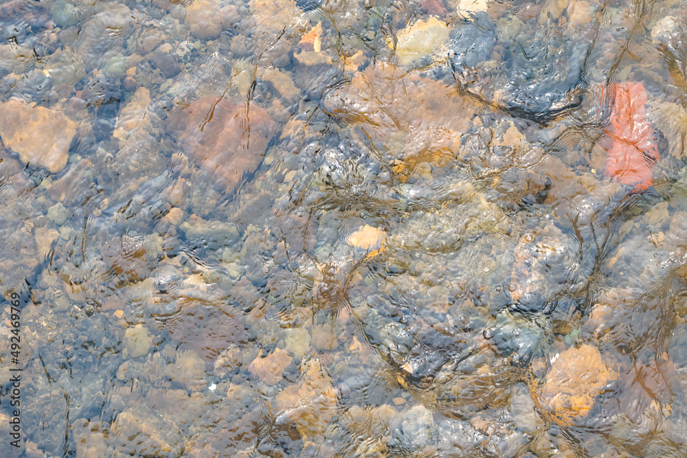 Water surface with rocks bottom in flowing stream, textured nature background photography